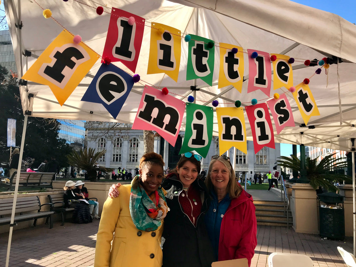 Three Little Feminist community members beneath a colorful Little Feminist banner