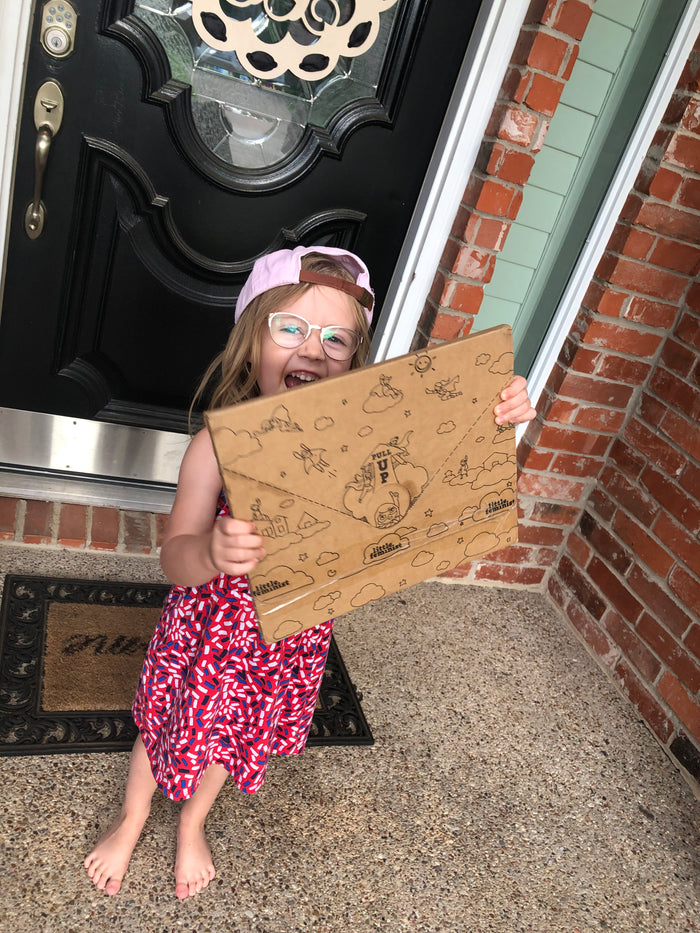 A child in a pink hat holding a Little Feminist box close to the camera
