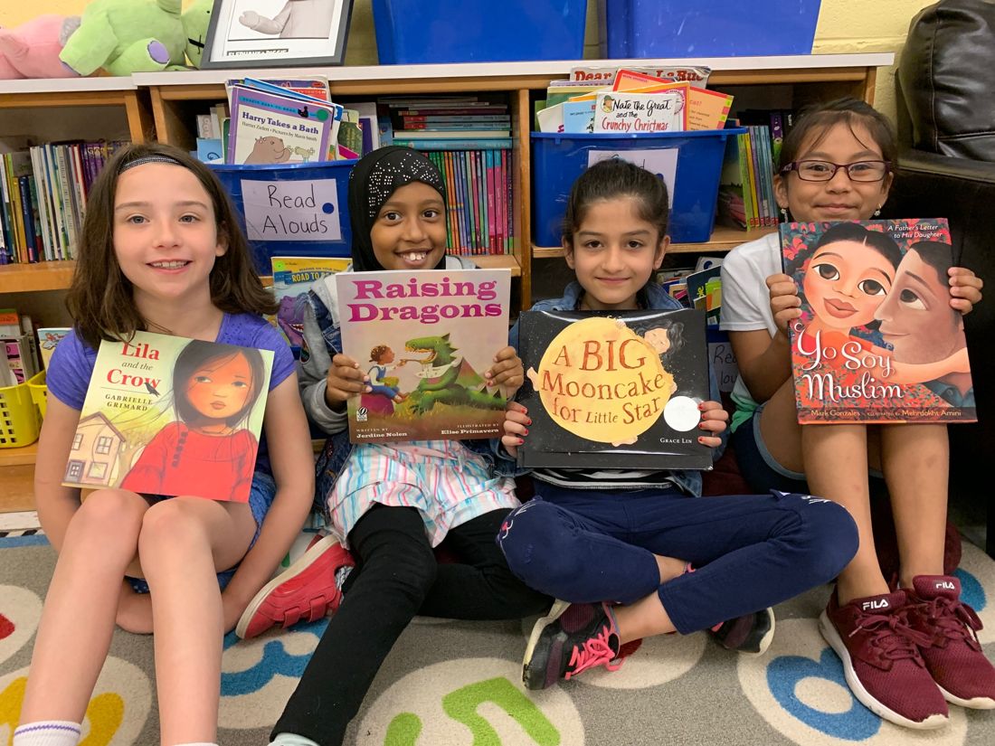 Four children holding their books in front of bookshelves