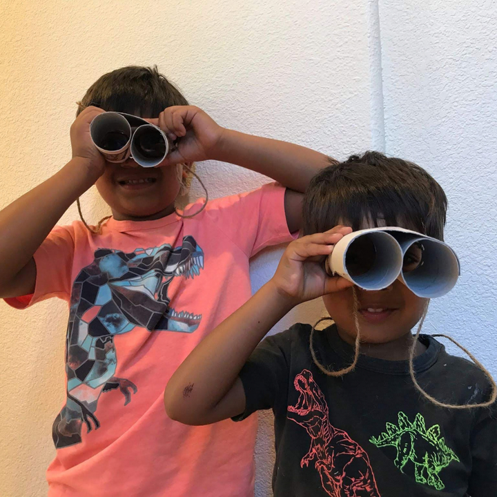 Two children looking through homemade cardboard binoculars.
