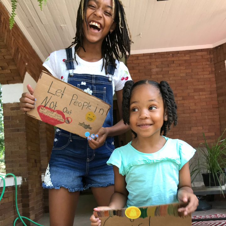 Two children holding handmade signs on a porch.