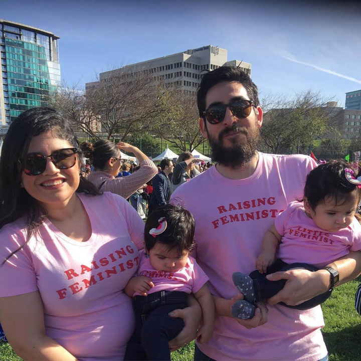 Two adults and two children wearing matching pink feminist shirts outdoors.