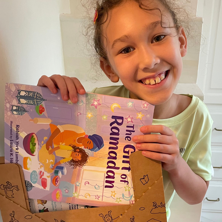 A smiling child holding The Gift of Ramadan.