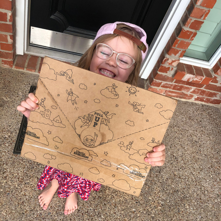 A smiling child holding a Little Feminist box.