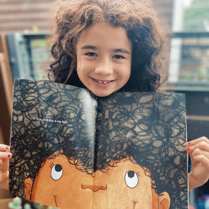 A child showing an illustrated book spread about hair.